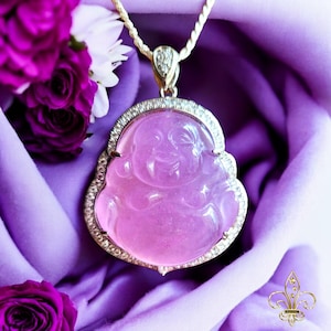 May include: A pink jade Buddha pendant with a diamond halo setting. The pendant is on a silver chain and is surrounded by purple flowers.