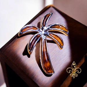 May include: A silver palm tree pendant with a brown wood inlay. The pendant is on a wooden surface.