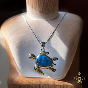 Può includere: Una collana d'argento con un ciondolo a forma di tartaruga in opale blu. La tartaruga è dettagliata con un guscio d'argento e un corpo d'argento.