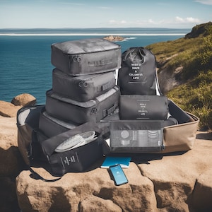 May include: A collection of dark gray packing cubes, a drawstring bag, and a cosmetic bag, all with the text "WISH U HAVE A COLORFUL LIFE". A pair of white sneakers and a notebook are also visible. The items are arranged on a rock with a scenic ocean backdrop.