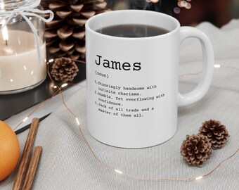 May include: White ceramic mug with a black handle. The mug has the word "James" printed on it, followed by the definition: "(noun) 1. Stunningly handsome with infinite charisma. 2. Humble. Yet overflowing with confidence. 3. Jack of all trade and a master of them all."