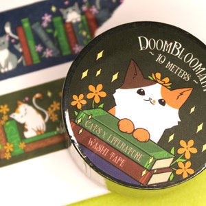 May include: A roll of washi tape featuring a calico cat with orange, white and brown fur. The cat is sitting on a stack of books with the text "Cats x Literature Washi Tape" and is surrounded by yellow flowers and sparkling stars. The background is dark green and the text "Doombloomart ~ 10 metres ~" is printed on the top right corner.