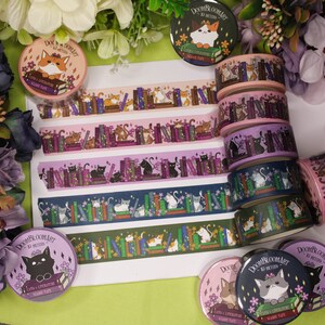 May include: A collection of colourful washi tapes featuring cats and books. The tapes are rolled up and arranged in a stack. The tapes are decorated with illustrations of cats reading books, cats sitting on books, and cats surrounded by books. The tapes are labelled "Doom & Bloom Art" and "Cats & Literature Washi Tape".