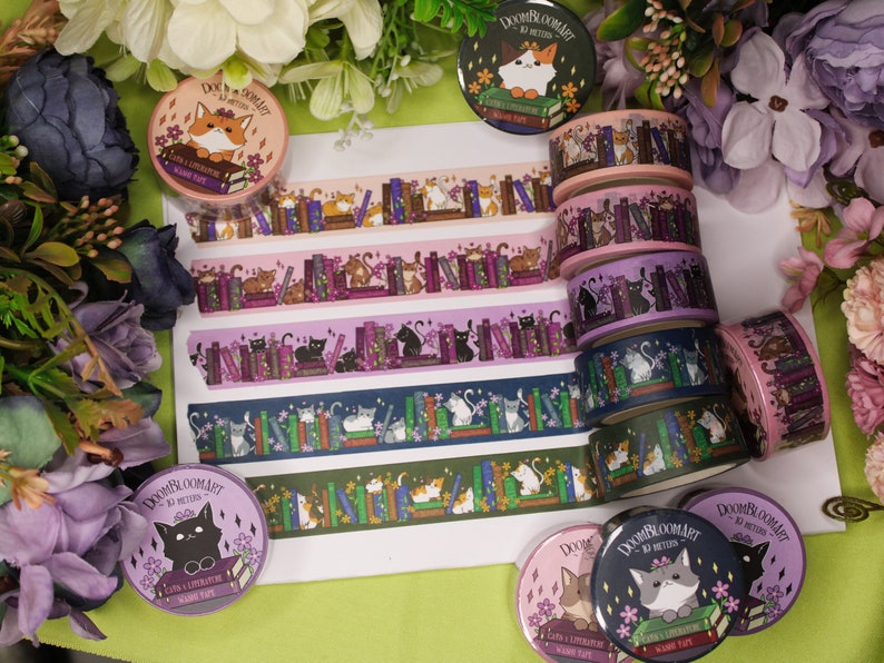 May include: A collection of colourful washi tapes featuring cats and books. The tapes are rolled up and arranged in a stack. The tapes are decorated with illustrations of cats reading books, cats sitting on books, and cats surrounded by books. The tapes are labelled "Doom & Bloom Art" and "Cats & Literature Washi Tape".