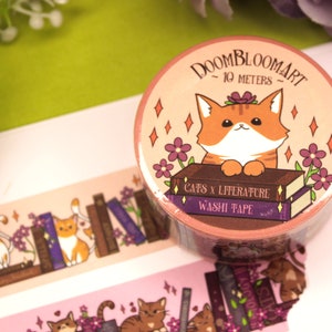 May include: A roll of pink and orange washi tape featuring a cute orange cat illustration. The tape has a stack of books with the text "Cats x Literature" and "Washi Tape". The tape is 10 metres long.
