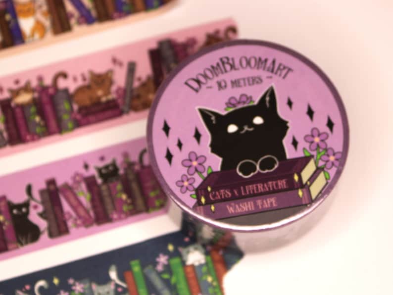 May include: Purple washi tape featuring a black cat perched on top of two books. The tape has a purple background with white flowers and black diamonds. The text on the tape reads "DOOMBLOOMART - 10 METERS - CATS & LITERATURE WASHI TAPE".