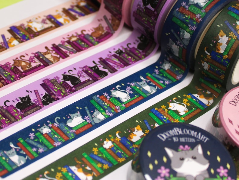 May include: A selection of colourful washi tapes featuring cats reading books. The tapes come in a range of colours and patterns, including purple, pink, blue, green, and brown. The cats are shown in various poses, some sitting, some standing, and some lying down. The books are stacked on shelves and have different titles. The tapes are labelled "DOOMBLOOMART - 10 METERS".