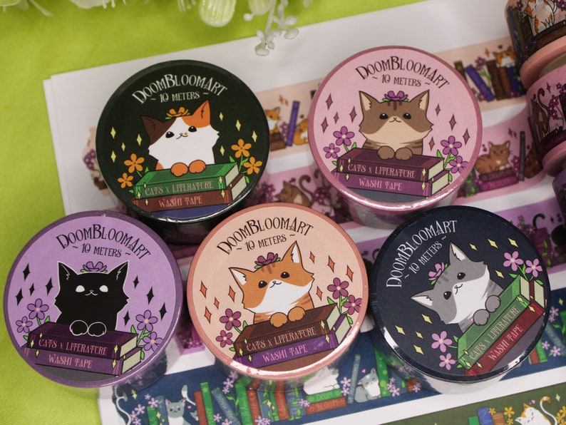 May include: Five rolls of washi tape featuring cats and books. Each roll has a different colour background and a different cat design. The text on the rolls reads "DOOMBLOOMART - 10 METERS - CATS & LITERATURE WASHI TAPE".