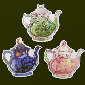 Puede incluir: Tres teteras decorativas con diferentes diseños. Una tetera tiene un diseño floral verde y blanco, otra tiene un diseño floral rosa y blanco, y la última tiene un diseño de noche estrellada azul y blanco.