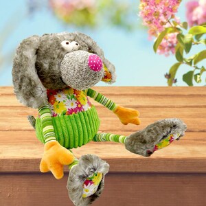 May include: A gray and green plush dog toy with a floral pattern on its chest. The dog has large, round eyes and a pink nose.