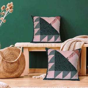 Könnte beinhalten: Zwei quadratische Zierkissen mit Patchwork-Design aus hellrosa Stoff, dunkelgrünem Stoff mit Paisley-Muster und einem dunkelgrün-weiß karierten Muster. Die Kissen haben eine dunkelgrüne Umrandung und einen Zierstreifen aus geblümtem Stoff.