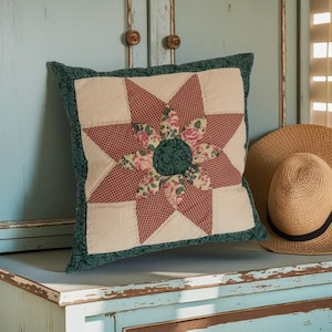 Può includere: Un cuscino quadrato con un motivo a stella centrale realizzato in tessuto a quadretti rosso e bianco, circondato da petali con stampa floreale e un centro verde scuro. Il cuscino presenta un bordo verde scuro paisley e fondo color crema.