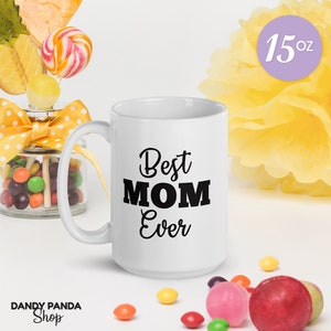 Op de afbeelding: Witte 15 oz mok met de zwarte tekst "Best MOM Ever". De mok wordt omringd door kleurrijke snoepjes, lolly's en een gele bloem. Het Dandy Panda Shop-logo is zichtbaar linksonder.
