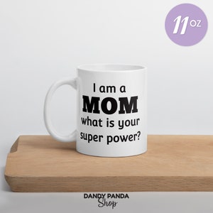 Op de afbeelding: Witte keramische mok met de tekst "I am a MOM what is your super power?" in het zwart. De mok is 325 ml en staat op een houten oppervlak. Het Dandy Panda Shop-logo staat onderaan.