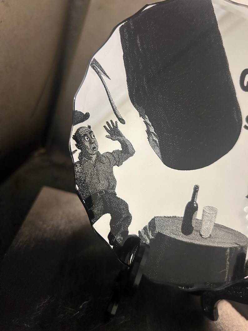 May include: A black and white illustration on a decorative mirror. The image depicts a man in a state of panic, with a large object falling towards him. A table with a bottle and glass is also visible.