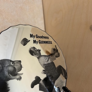 K&ouml;nnte beinhalten: Ein dekorativer Teller mit einer Schwarz-Wei&szlig;-Illustration, die einen Mann zeigt, der vor einem b&auml;renartigen Wesen flieht. Der Teller tr&auml;gt den Text "My Goodness My Guinness".