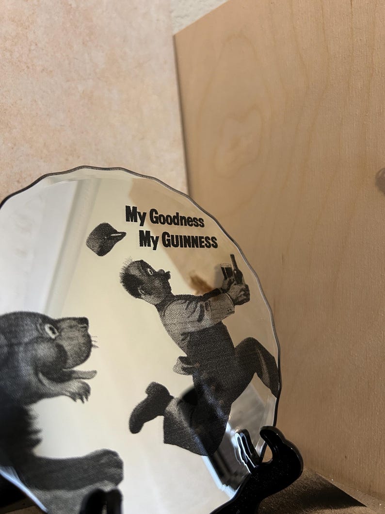 K&ouml;nnte beinhalten: Ein dekorativer Teller mit einer Schwarz-Wei&szlig;-Illustration, die einen Mann zeigt, der vor einem b&auml;renartigen Wesen flieht. Der Teller tr&auml;gt den Text "My Goodness My Guinness".