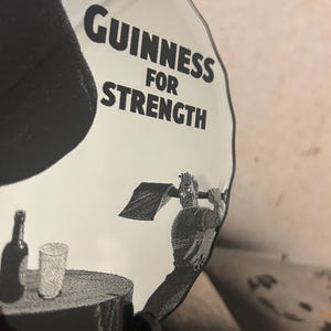 May include: A clear, decorative glass plate with the words "Guinness For Strength" in bold black letters. The plate features a black and white illustration of a man swinging a shovel, with a bottle and glass on a table.