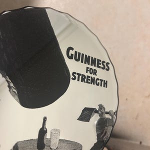 May include: A white and black Guinness advertisement featuring the text "Guinness for Strength." The image shows a man swinging an axe, a bottle, and a glass on a table.
