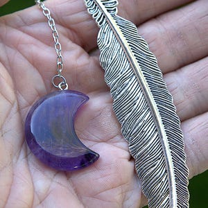 Puede incluir: Un marcapáginas de pluma de plata con un dije de cristal de amatista en forma de media luna que cuelga de una cadena de plata.