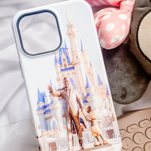 May include: White iPhone case featuring a colourful image of Cinderella's Castle at Walt Disney World, with Walt Disney and Mickey Mouse in front of the castle.