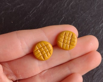 May include: A pair of yellow, round, textured earrings. The earrings have a grid pattern.