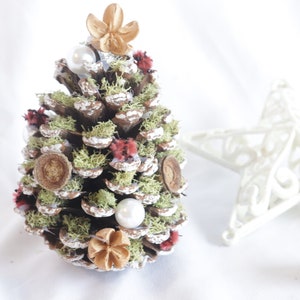 May include: A small pine cone Christmas tree decorated with white beads, red and white felt flowers, and brown wood slices.