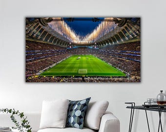 May include: A rectangular wall art print depicting a wide-angle view of a crowded football stadium at night. The bright green pitch is surrounded by packed stands, with golden fireworks erupting from the stadium roof into the dark blue sky.