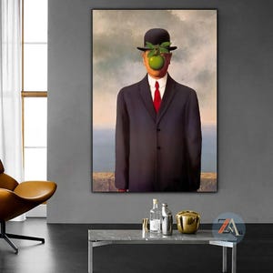 May include: A framed wall art print depicting a person in a dark suit, white shirt, and red tie, wearing a black bowler hat. A bright green apple with leaves obscures the face. The background shows a cloudy sky above a stone wall and sea.