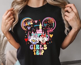 May include: Black t-shirt with a colorful graphic of Mickey Mouse and Daisy Duck in front of Cinderella's Castle. The text "Girls Trip" is below the graphic.