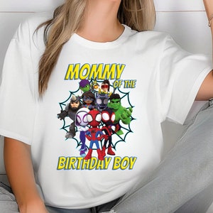 Puede incluir: Camiseta blanca con un gr&aacute;fico colorido de superh&eacute;roes de dibujos animados, incluyendo a Spider-Man y Hulk. El texto "MOMMY OF THE BIRTHDAY BOY" est&aacute; impreso en amarillo con un contorno azul. Un dise&ntilde;o alegre y festivo.