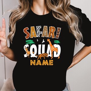 以下が含まれることがあります： 「サファリ・スクワッド」というカラフルなグラフィックがプリントされた黒いTシャツ。キリン、トラ、鹿が描かれています。「NAME」という文字がグラフィックの下にあります。