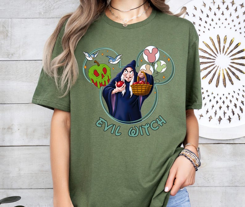 May include: Green t-shirt featuring a graphic of the Evil Queen from Snow White. The graphic depicts the Evil Queen holding a basket of apples and a Mickey Mouse head silhouette with birds and apples. The text "Evil Witch" is printed below the graphic.