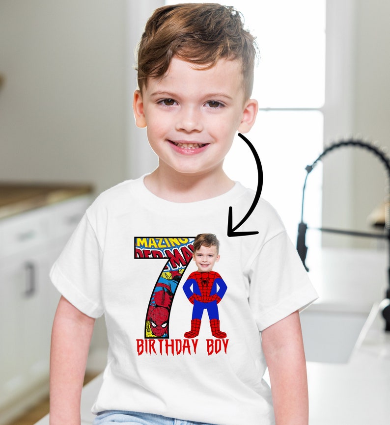 Op de afbeelding: Wit T-shirt met een rood en blauw nummer 7 met een stripboekontwerp en de woorden "Amazing Spiderman" en "Birthday Boy". Het gezicht van een kind is over het Spiderman-personage gelegd.