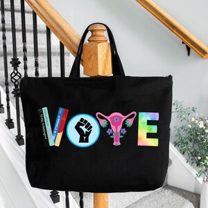 May include: Black tote bag with the word "VOTE" in colorful letters and graphics. The "V" is made of books, the "O" has a raised fist, the "T" has a uterus graphic, and the "E" is rainbow-colored.