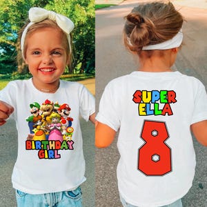 May include: White t-shirt with a colorful graphic of Mario characters and the text "Birthday Girl". The back of the shirt has the text "Super Ella" and the number "8" in red.