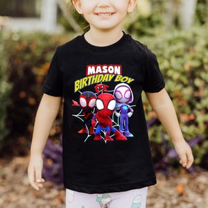 Puede incluir: Camiseta negra con un gr&aacute;fico de tres personajes de Spider-Man de dibujos animados. El texto "MASON BIRTHDAY BOY" est&aacute; impreso en amarillo en la camiseta.