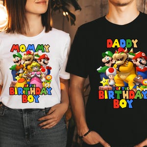 May include: White and black t-shirts with a graphic of Mario characters. The white shirt says "Mommy of the Birthday Boy" and the black shirt says "Daddy of the Birthday Boy".