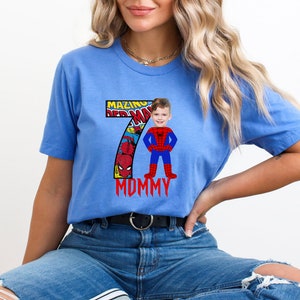 Op de afbeelding: Een blauw T-shirt met een nummer 7 gemaakt van comic book panelen met Spiderman. Het nummer 7 heeft de woorden "Mazing" en "Mommy" erop. Het gezicht van een kind is over het Spiderman-personage gelegd.