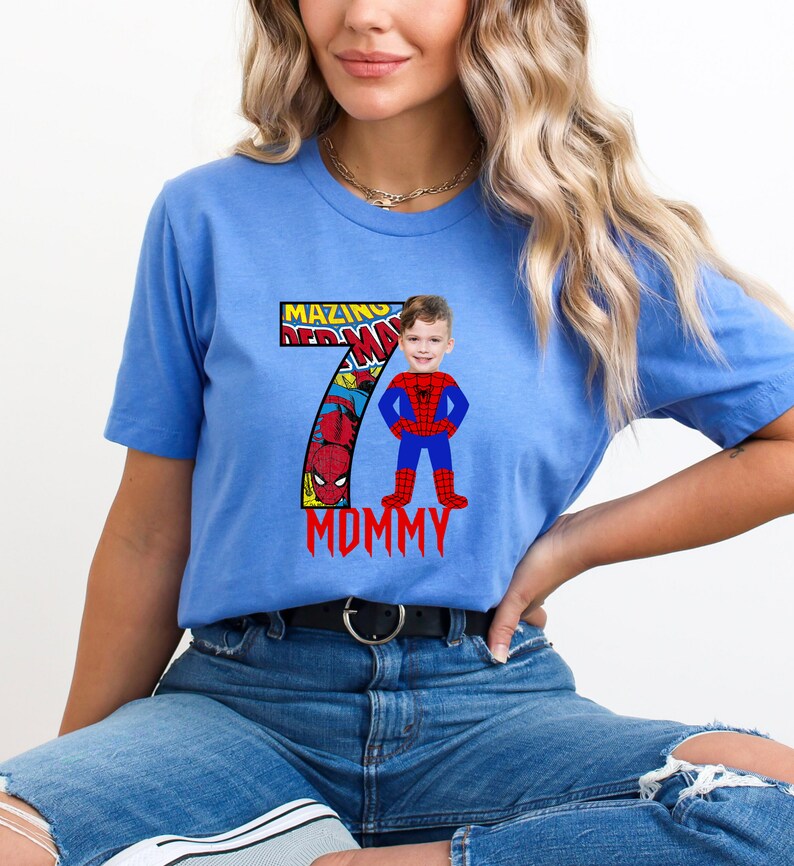 Op de afbeelding: Een blauw T-shirt met een nummer 7 gemaakt van comic book panelen met Spiderman. Het nummer 7 heeft de woorden "Mazing" en "Mommy" erop. Het gezicht van een kind is over het Spiderman-personage gelegd.