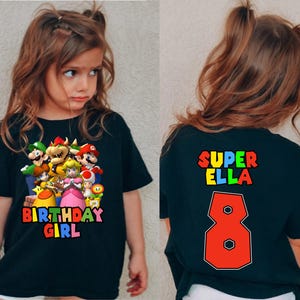 May include: Black t-shirt with a colorful Super Mario Bros. graphic on the front and the text "SUPER ELLA 8" on the back.