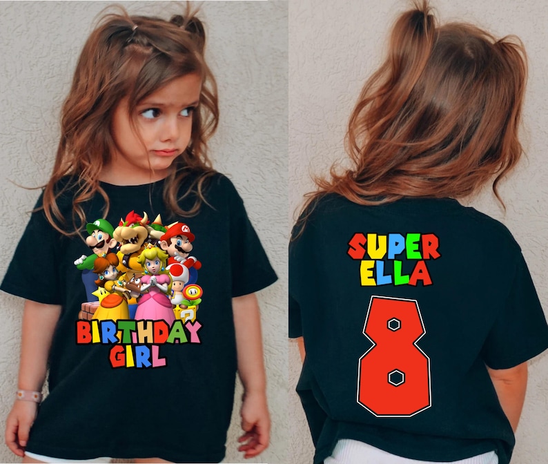 May include: Black t-shirt with a colorful Super Mario Bros. graphic on the front and the text "SUPER ELLA 8" on the back.