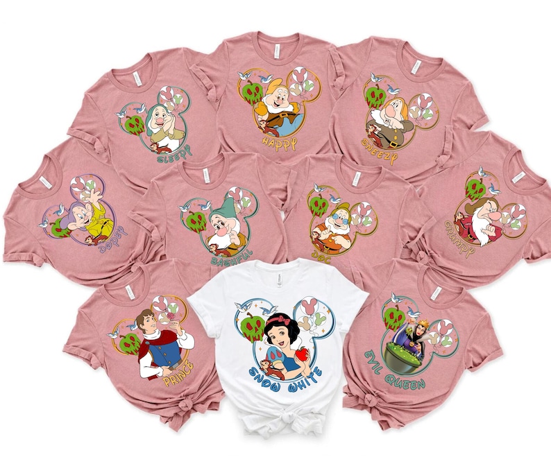 May include: Set of ten pink t-shirts featuring different Disney characters from Snow White. Each shirt depicts a different character with a Mickey Mouse ear design and text. The text on the shirts includes "Sleepy", "Happy", "Grumpy", "Dopey", "Sneezy", "Bashful", "Doc", "Evil Queen", "Snow White", and "Prince".
