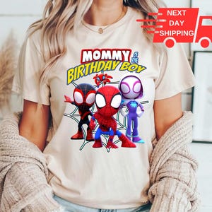 Puede incluir: Una camiseta blanca con un gr&aacute;fico de personajes de Spider-Man. El texto "Mommy of the Birthday Boy" est&aacute; impreso en amarillo y negro.