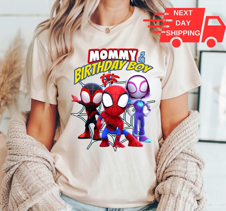 Puede incluir: Una camiseta blanca con un gr&aacute;fico de personajes de Spider-Man. El texto "Mommy of the Birthday Boy" est&aacute; impreso en amarillo y negro.