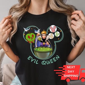 May include: Black t-shirt featuring a graphic of the Evil Queen from Snow White holding a cauldron. The graphic is in the shape of Mickey Mouse's head with a green apple and birds. The text "Evil Queen" is below the graphic.