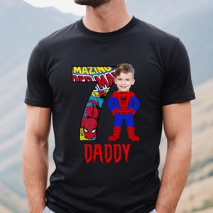 Op de afbeelding: Zwart T-shirt met een rood nummer 7 met een stripboekbeeld van Spiderman. Het gezicht van een kind is over het Spiderman-personage gelegd. De tekst "AMAZING" en "DADDY" staat op het shirt gedrukt.
