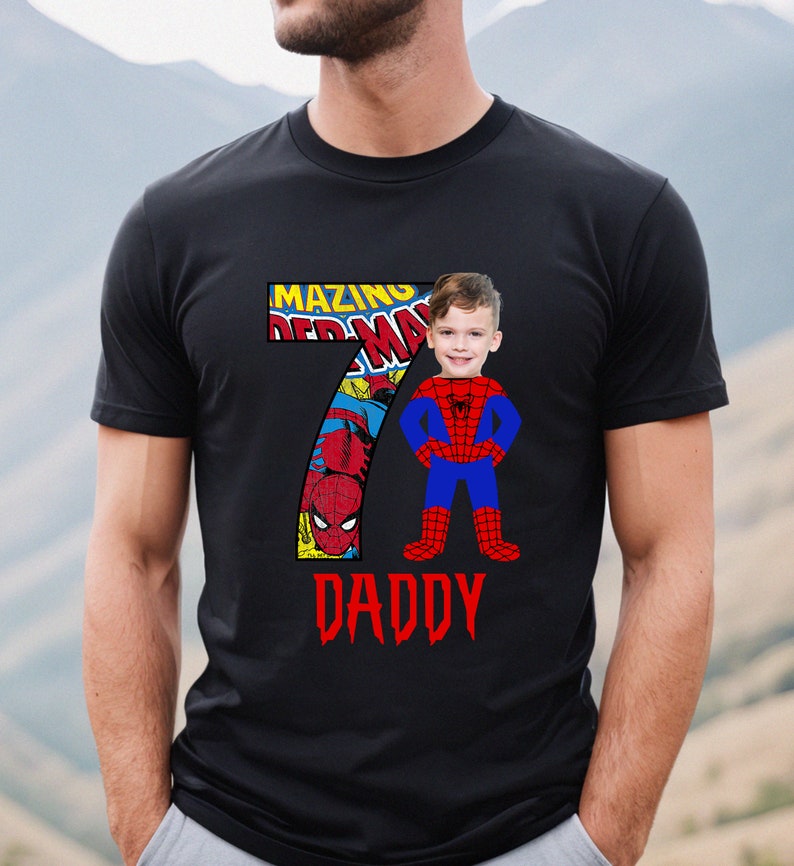 Op de afbeelding: Zwart T-shirt met een rood nummer 7 met een stripboekbeeld van Spiderman. Het gezicht van een kind is over het Spiderman-personage gelegd. De tekst "AMAZING" en "DADDY" staat op het shirt gedrukt.