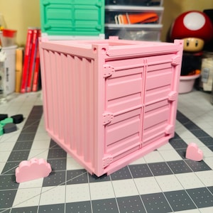 May include: A pink miniature shipping container with a closed door. The container is made of plastic and has a realistic design.