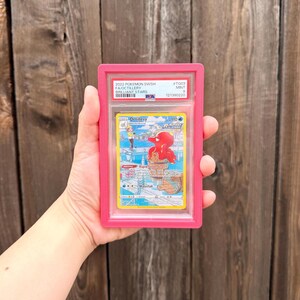 May include: A PSA graded 2022 Pokemon SWSH Brilliant Stars Octillery trading card in a bright pink plastic slab. The card features a red Octillery character in a fishing scene with text including Octillery, Rapid Strike, and 110 HP.
